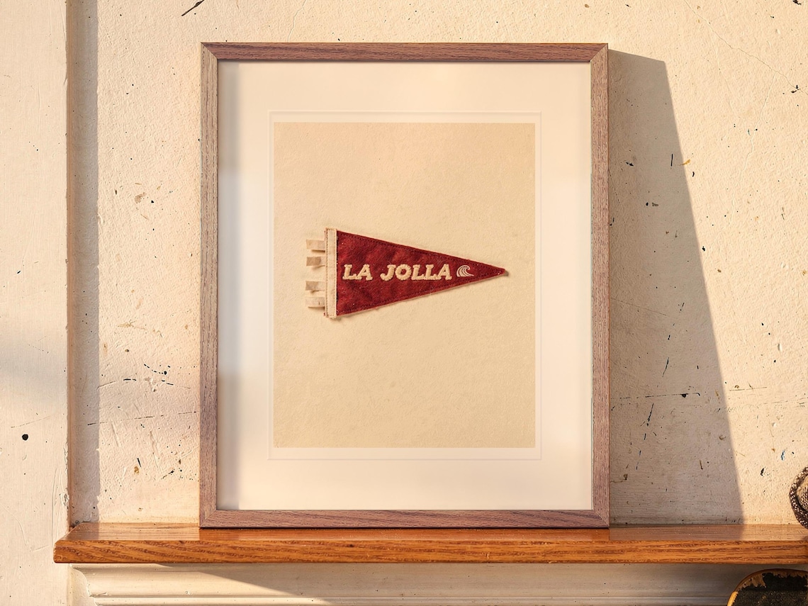 La Jolla Surf Pennant print in a Red Oak frame with a white mat, leaning on the ledge against the wall in a hallway.