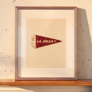 La Jolla Surf Pennant print in a Red Oak frame with a white mat, leaning on the ledge against the wall in a hallway.