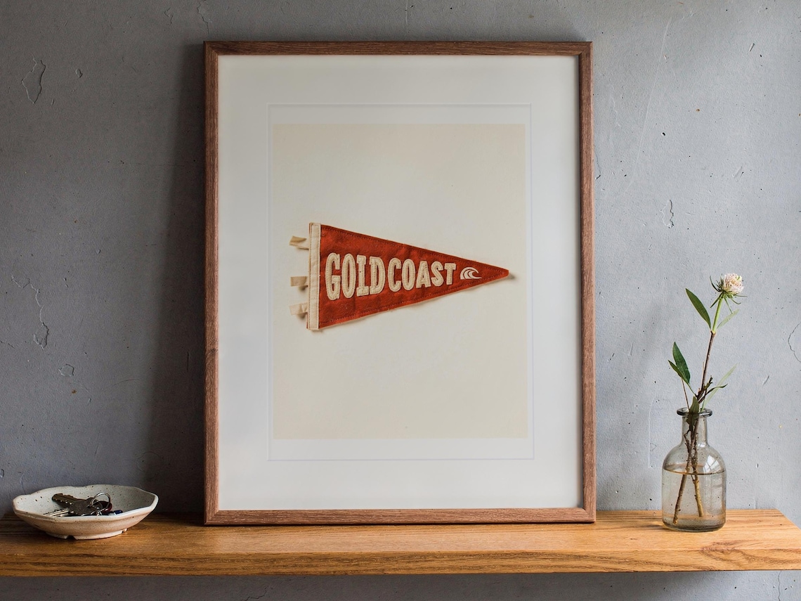 Gold Coast printable art, shown printed in a Red Oak frame with a white mat, leaning on the ledge against the wall in a hallway.