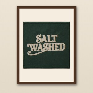 Pode incluir: Uma obra de arte emoldurada com um quadrado verde escuro com as palavras "SALT WASHED" em uma fonte decorativa creme. A obra de arte é definida contra um fundo branco dentro de uma moldura marrom.