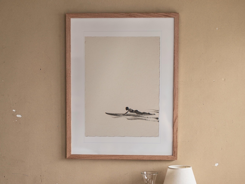 Paddling Surfer Ink Style print in a Red Oak frame with a white mat, hanging above the bedside table in a calm bedroom.