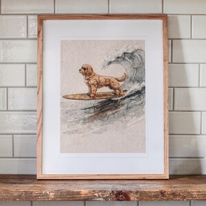Goldendoodle Surfing printable art, shown printed in a Red Oak frame with a white mat, leaning on the shelf against the wall in a cottage kitchen.