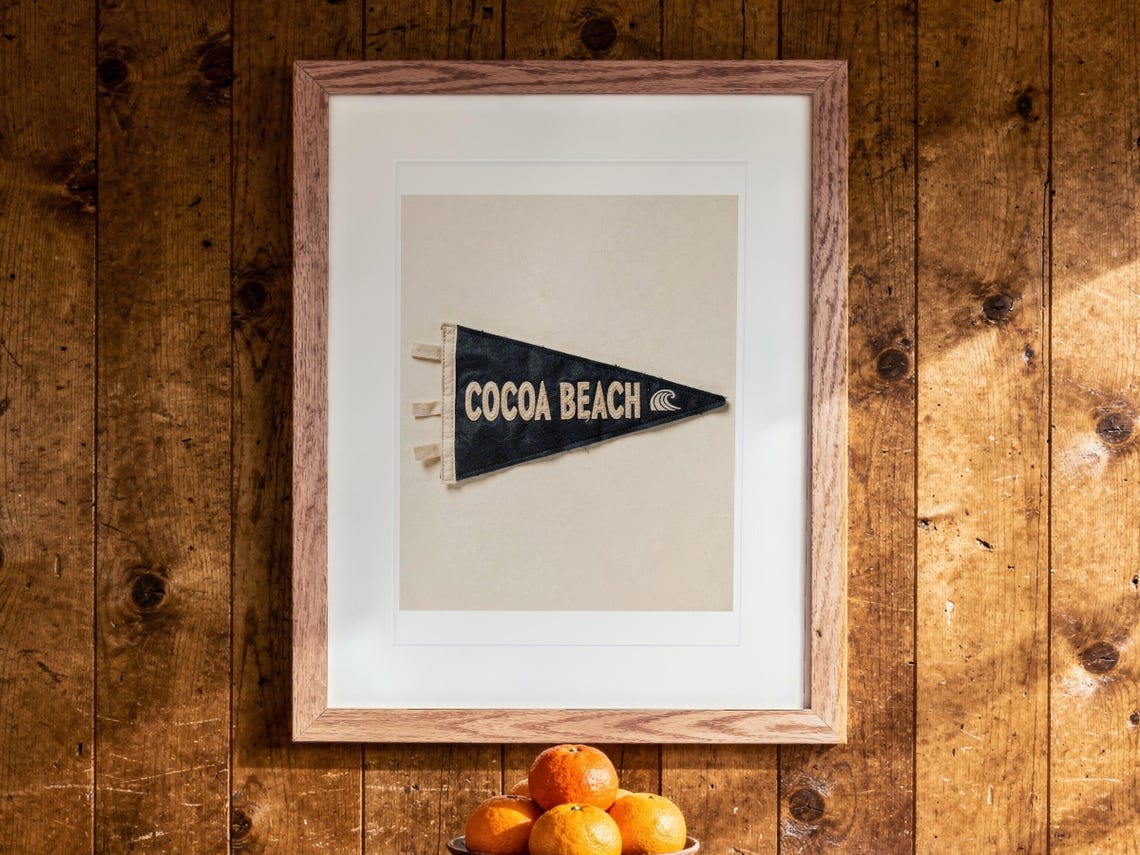 Cocoa Beach Surf Pennant print in a Red Oak frame with a white mat, hanging above the cabinet in a game room.