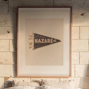 Nazaré Surf Pennant print in a Red Oak frame with a white mat, hanging above the bed in a surf shack bedroom.