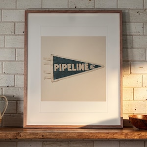 Pipeline Surf Pennant print in a Red Oak frame with a white mat, leaning on the shelf against the wall in a cottage kitchen.