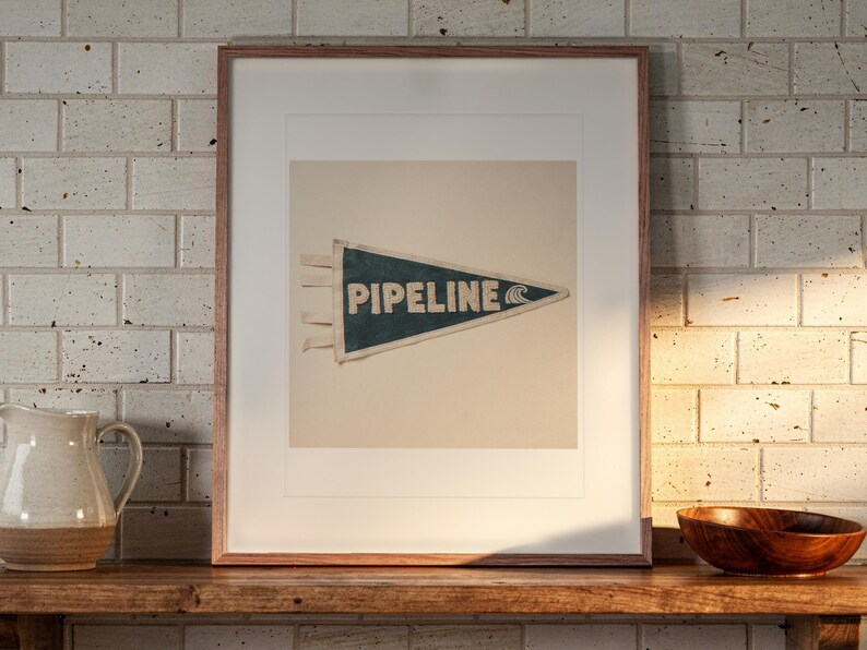 Pipeline Surf Pennant print in a Red Oak frame with a white mat, leaning on the shelf against the wall in a cottage kitchen.