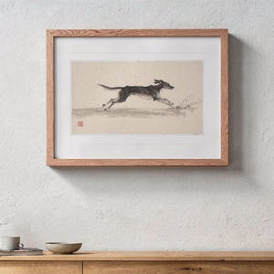 Puede incluir: Una impresión horizontal enmarcada que muestra a un perro negro y marrón en plena carrera. La obra está realizada en estilo boceto sobre un fondo beige claro con un pequeño sello cuadrado rojo en la esquina inferior izquierda, dentro de un marco de madera clara.