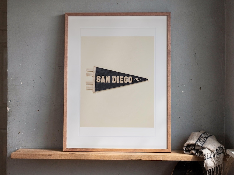 San Diego Surf Pennant print in a Red Oak frame with a white mat, leaning on the ledge against the wall in a hallway.