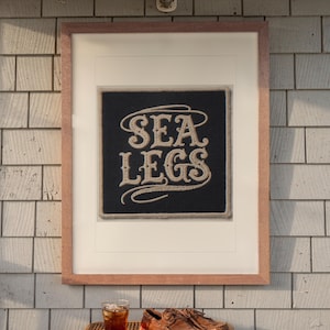 Sea Legs Patch print in a Red Oak frame with a white mat, hanging above the table in a screened beach porch.