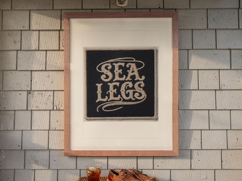 Sea Legs Patch print in a Red Oak frame with a white mat, hanging above the table in a screened beach porch.