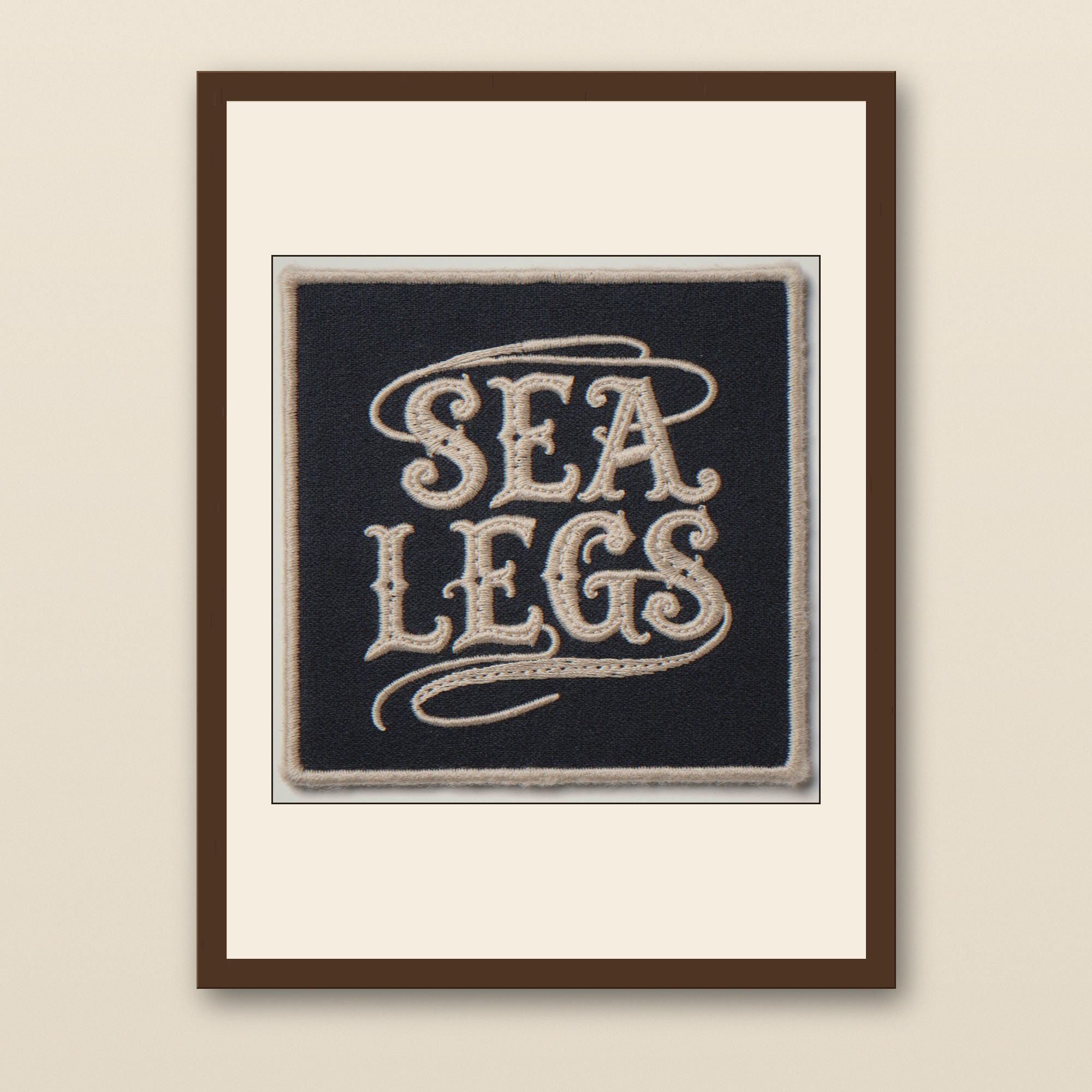 Sea Legs Embroidered Patch Print - walnut framed art print with cream mat on plaster wall
