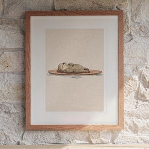 Sea Otter on Surfboard print in a Red Oak frame with a white mat, hanging above the console in a sunroom.
