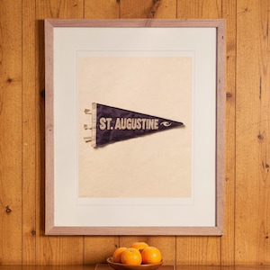 St. Augustine Surf Pennant print in a Red Oak frame with a white mat, hanging above the cabinet in a game room.