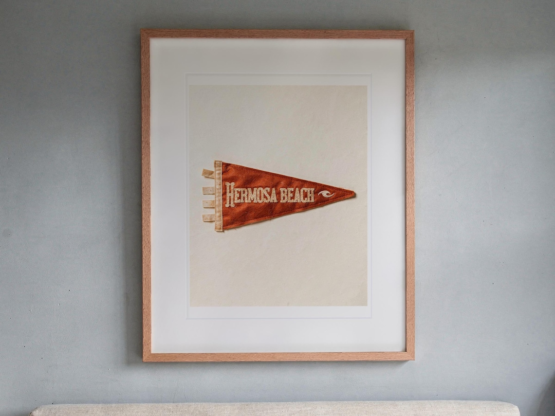 Hermosa Beach Surf Pennant print in a Red Oak frame with a white mat, hanging above the headboard in a calm bedroom.