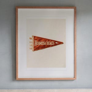 Hermosa Beach Surf Pennant print in a Red Oak frame with a white mat, hanging above the headboard in a calm bedroom.