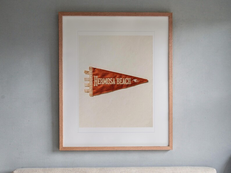 Hermosa Beach Surf Pennant print in a Red Oak frame with a white mat, hanging above the headboard in a calm bedroom.