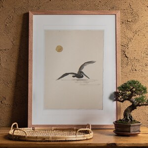 Flying Pelican Ink Style print in a Red Oak frame with a white mat, leaning against the wall above the tea table in a tea room.