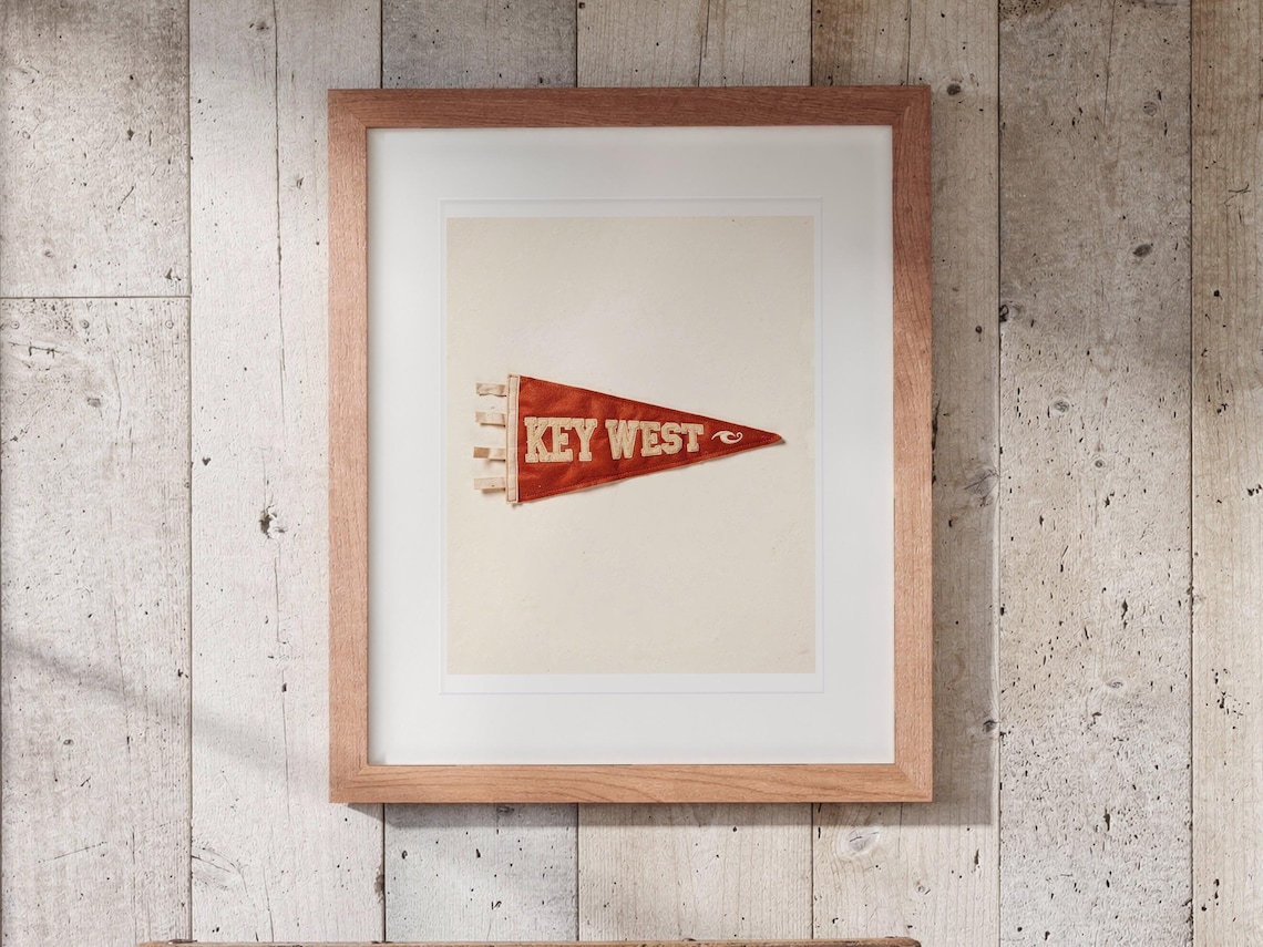Key West Surf Pennant print in a Red Oak frame with a white mat, hanging above the trunk in a beach house loft.
