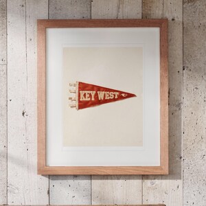 Key West Surf Pennant print in a Red Oak frame with a white mat, hanging above the trunk in a beach house loft.