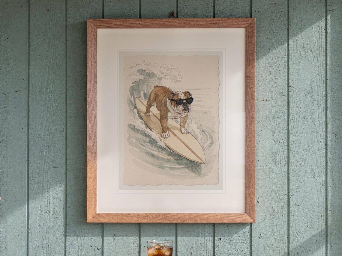 Bulldog Surfing print in a Red Oak frame with a white mat, hanging above the table in a screened beach porch.