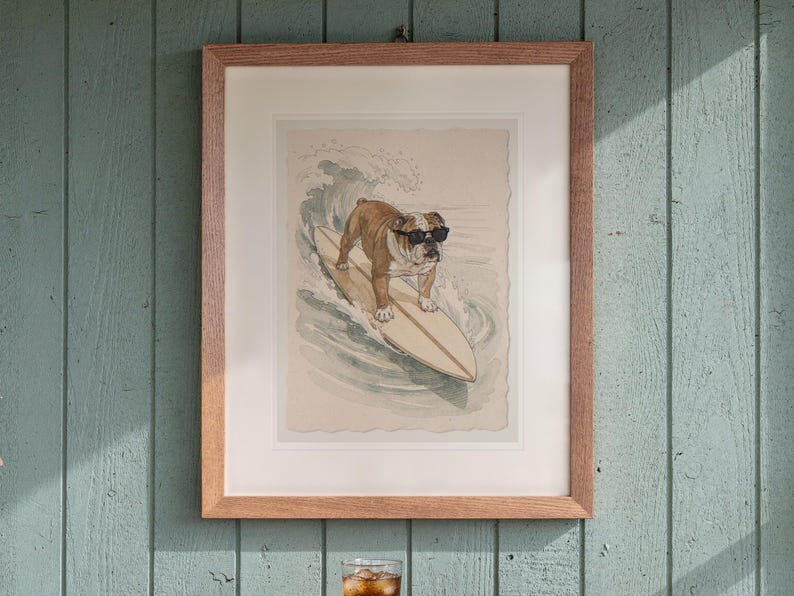 Bulldog Surfing print in a Red Oak frame with a white mat, hanging above the table in a screened beach porch.