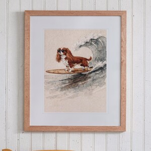 Cavalier King Charles Spaniel Surfing print in a Red Oak frame with a white mat, hanging above the bookshelf in a kids' room.