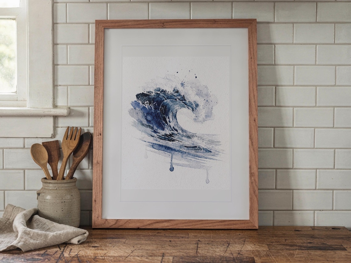Prussian Blue Wave Watercolor print in a Red Oak frame with a white mat, leaning on the counter against the backsplash in a cottage kitchen.