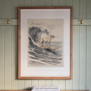 May include: A framed art print featuring a light-colored dog wearing sunglasses while standing on a surfboard riding a large ocean wave. The illustration uses shades of blue, gray, and tan, enclosed in a simple wooden frame with a white mat.