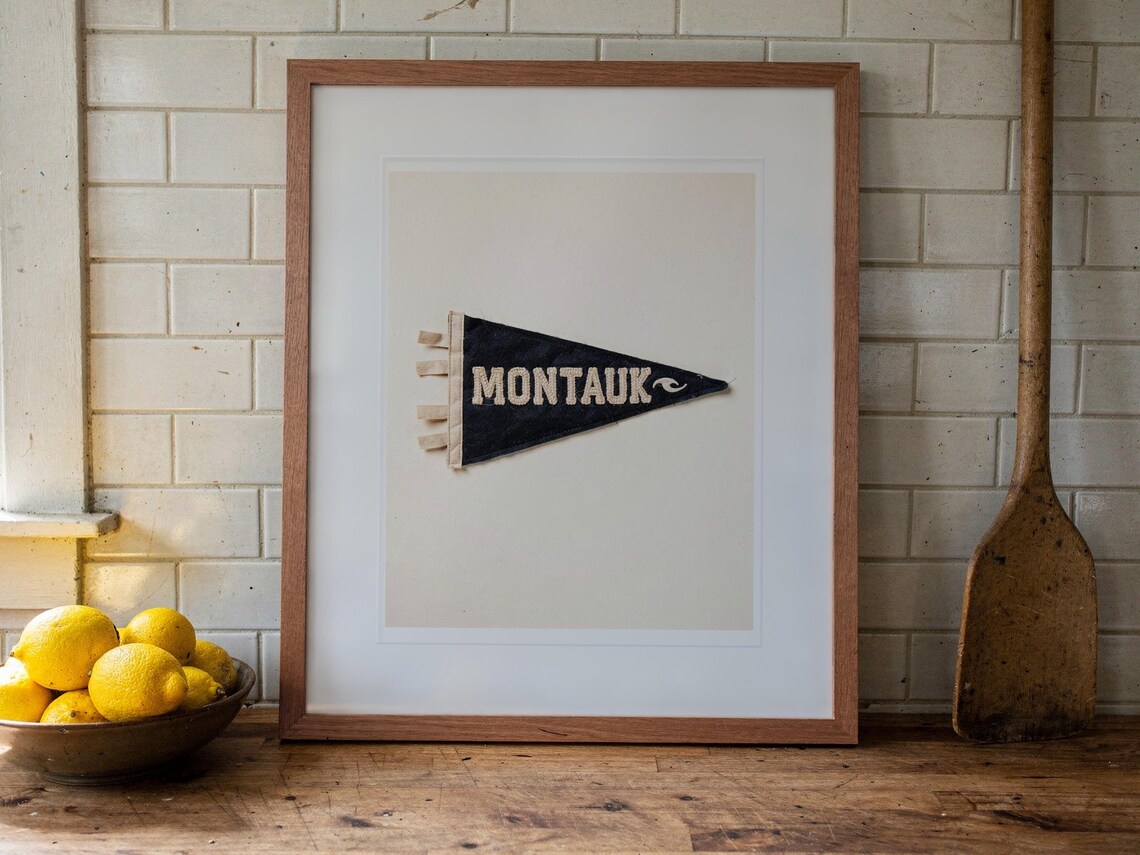 Montauk Surf Pennant print in a Red Oak frame with a white mat, leaning on the counter against the backsplash in a cottage kitchen.