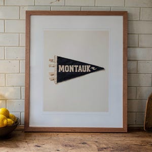 Montauk Surf Pennant print in a Red Oak frame with a white mat, leaning on the counter against the backsplash in a cottage kitchen.