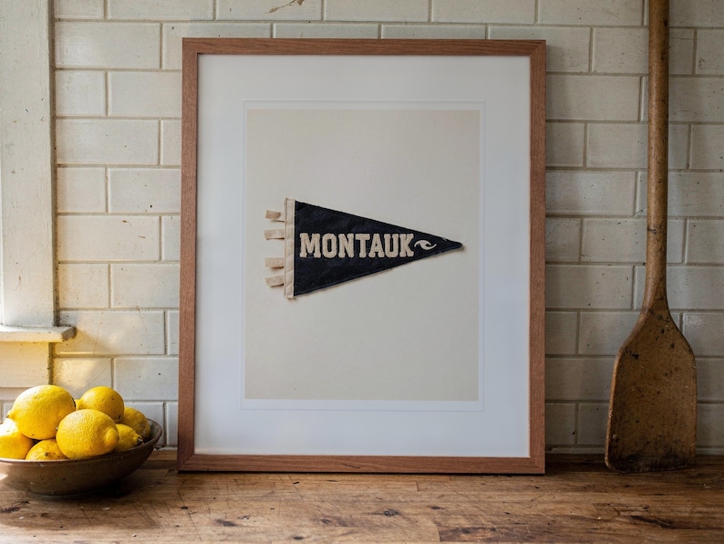 Montauk Surf Pennant print in a Red Oak frame with a white mat, leaning on the counter against the backsplash in a cottage kitchen.