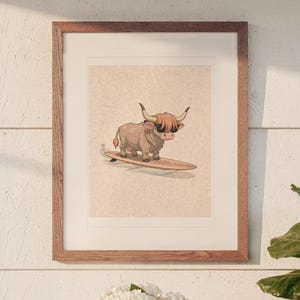 May include: A framed wall art print featuring a cartoon illustration of a brown Highland cow wearing black sunglasses while standing on a wooden surfboard. The artwork is set against a light beige, textured background within a wooden frame.