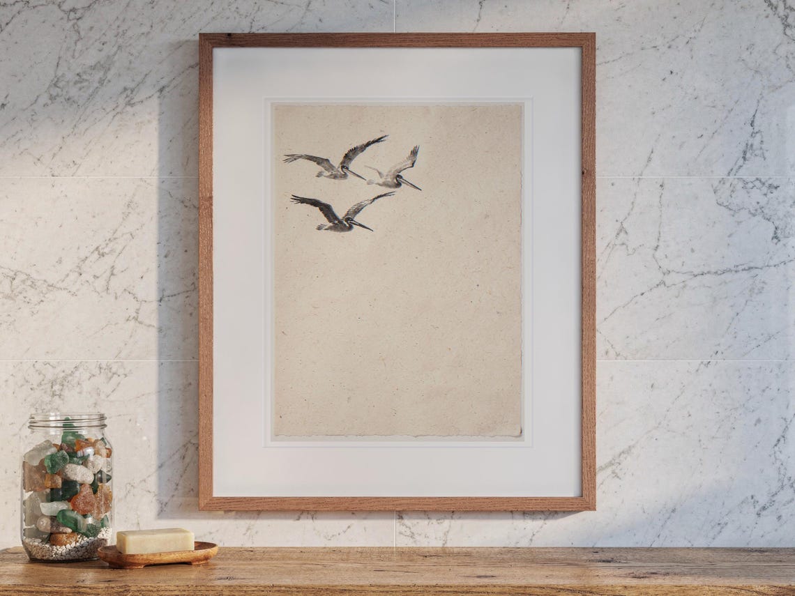 Flying Pelicans Ink Style print in a Red Oak frame with a white mat, hanging above the vanity in a bright bathroom.