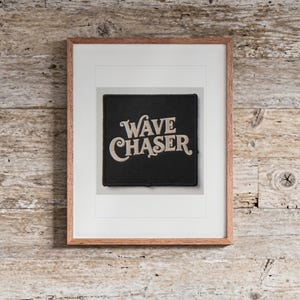 Wave Chaser Patch print in a Red Oak frame with a white mat, hanging above the bench in a beach house loft.