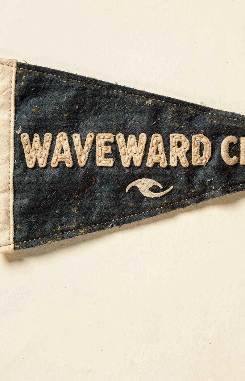 Close detail of the Waveward Club pennant texture, cream lettering, and vintage finish