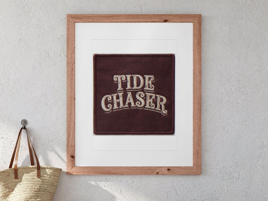 Tide Chaser Patch print in a Red Oak frame with a white mat, hanging above the bench in a beach cottage entryway.
