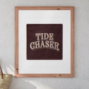 Tide Chaser Patch print in a Red Oak frame with a white mat, hanging above the bench in a beach cottage entryway.