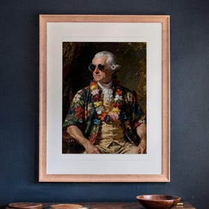 May include: A framed portrait print featuring a historical figure wearing a floral print shirt, a colorful lei, and dark sunglasses. The artwork is encased in a light-colored wooden frame with a white mat, displayed against a dark wall.