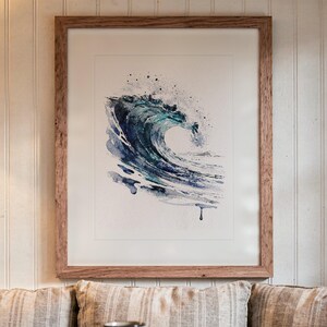 May include: A framed watercolor painting of a crashing ocean wave in shades of deep blue, teal, and white. The artwork features expressive paint splatters and fluid brushstrokes, encased in a simple, light-toned wooden frame with a white mat.