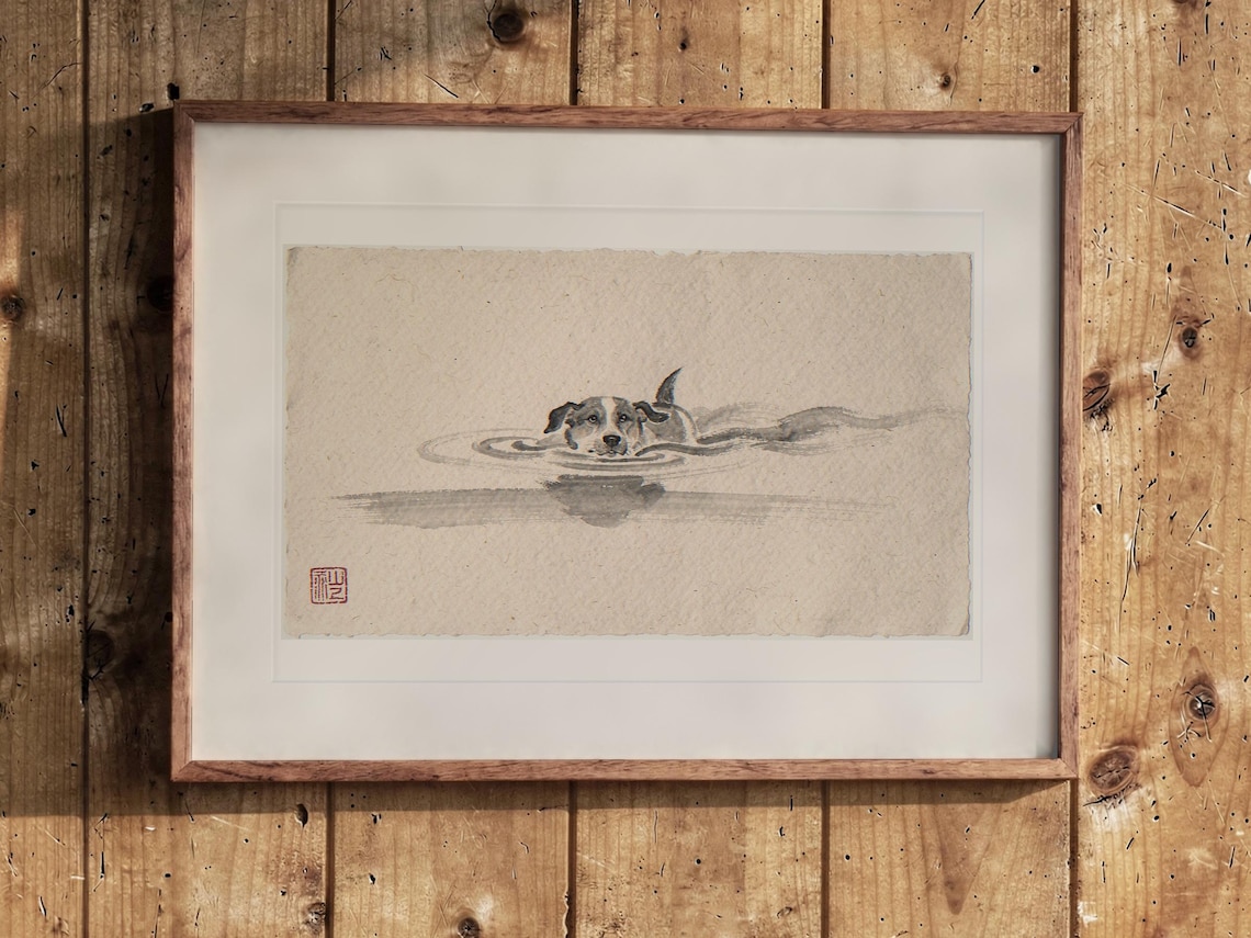 Swimming Dog Xieyi Ink print in a Red Oak frame with a white mat, leaning against the wall above the tea table in a tea room.