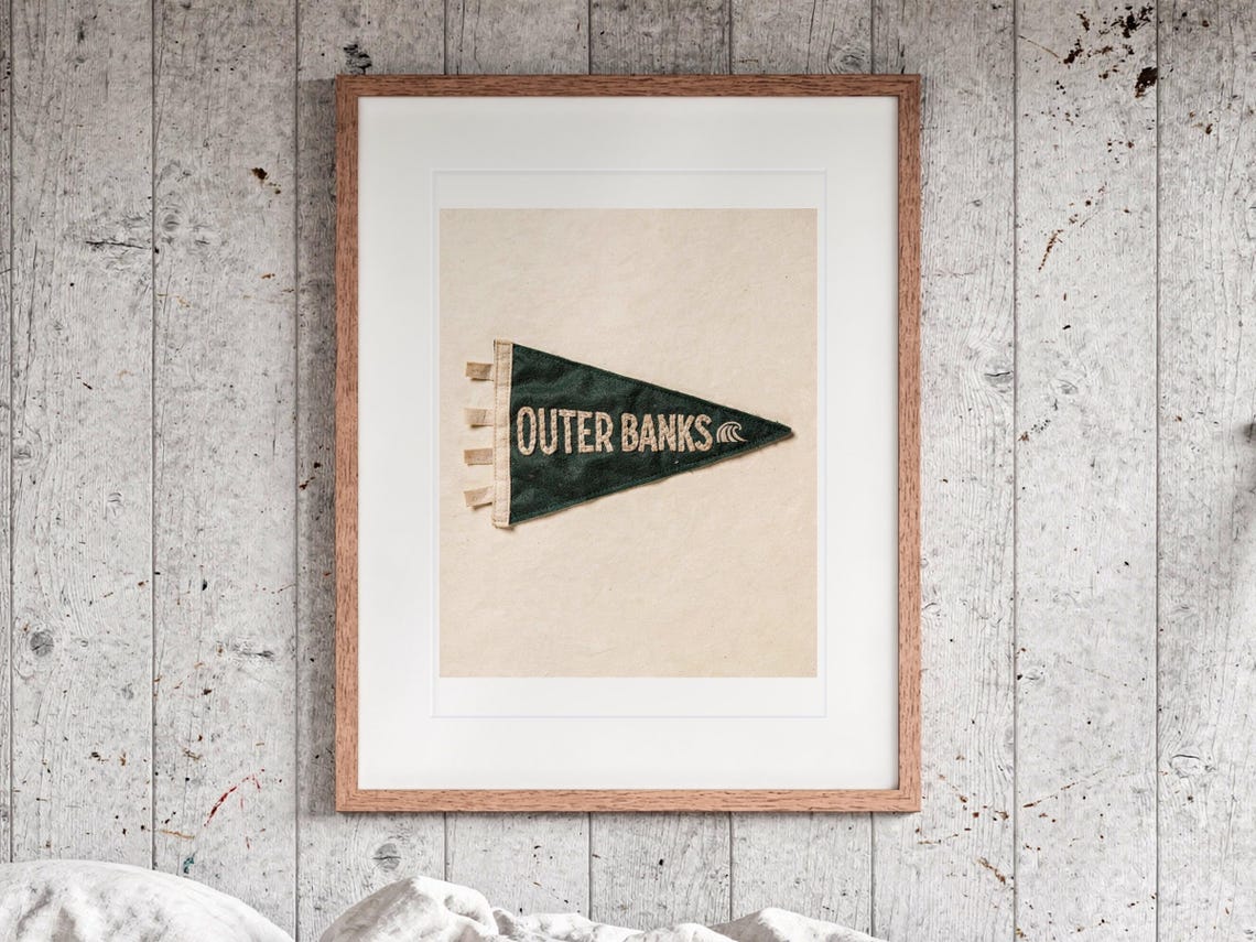 Outer Banks Surf Pennant print in a Red Oak frame with a white mat, hanging above the bed in a surf shack bedroom.