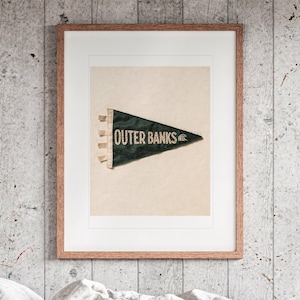 Outer Banks Surf Pennant print in a Red Oak frame with a white mat, hanging above the bed in a surf shack bedroom.