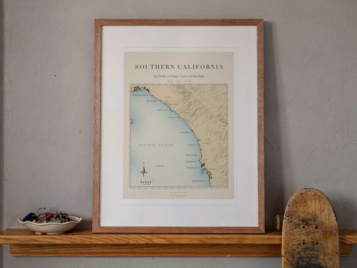 Southern California Surf Map print in a Red Oak frame with a white mat, leaning on the ledge against the wall in a hallway.