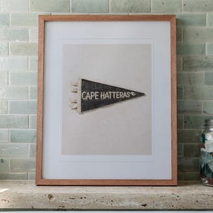 Cape Hatteras print in a Red Oak frame with a white mat, leaning on the ledge against the wall in a bright bathroom.