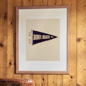 Bondi Beach print in a Red Oak frame with a white mat, hanging on the paneling in a 1960s den.