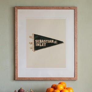 Sebastian Inlet Surf Pennant print in a Red Oak frame with a white mat, hanging above the sideboard in a dining room.