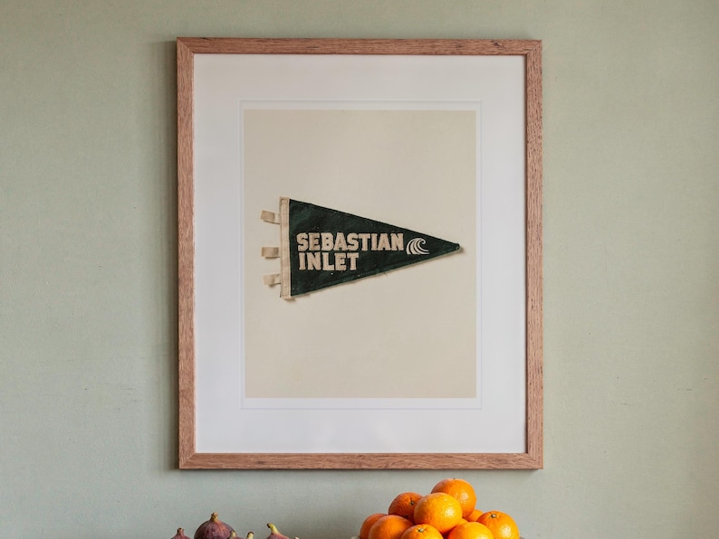 Sebastian Inlet Surf Pennant print in a Red Oak frame with a white mat, hanging above the sideboard in a dining room.