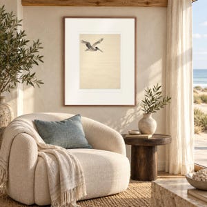 Flying Pelican Ink Style print in a Red Oak frame with a white mat in a light-filled coastal sitting room.
