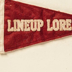 Close detail of the Lineup Lore pennant texture, cream lettering, and vintage finish