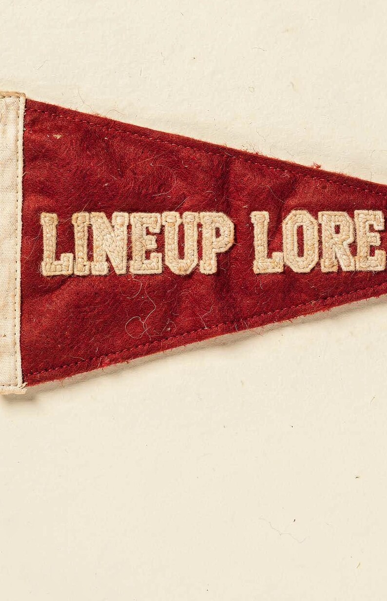 Close detail of the Lineup Lore pennant texture, cream lettering, and vintage finish
